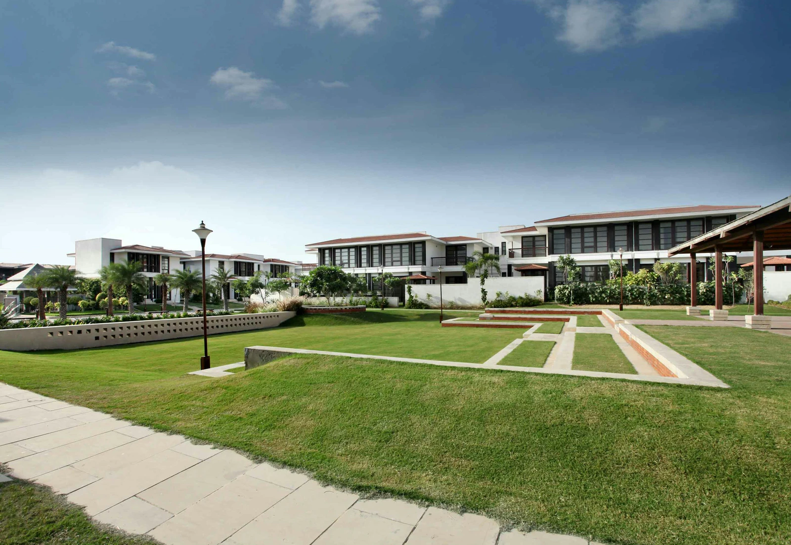 Independent low-rise villas arranged around a broad lawn and stone paths at Tatvam Villas in Gurugram